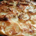 Potatoes au gratin in a white baking dish with golden bubbling cheese crust and creamy layers visible