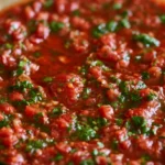 red chimichurri sauce in a small bowl drizzled over grilled steak on a white plate