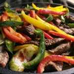 Blackstone steak fajitas with charred peppers and onions on a sizzling griddle