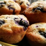 Blueberry muffins recipe showing golden domed muffins with bursting berries on a white plate