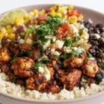 Chipotle bowl with cilantro lime rice, smoky grilled chicken, black beans, fresh pico de gallo, shredded cheese, and creamy guacamole on a white plate