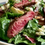 Steak salad with sliced ribeye, mixed greens, cherry tomatoes, cucumber, and avocado drizzled with balsamic vinaigrette on a white plate
