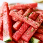 Watermelon fries arranged on white platter with coconut lime dip in small bowl