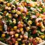 Cowboy caviar in a white serving bowl with colorful beans, corn, tomatoes, and bell peppers topped with fresh cilantro