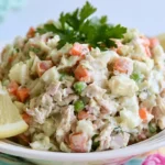 Chicken salad recipe served in a white bowl with fresh lettuce and tomatoes on a wooden table