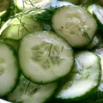 German cucumber salad with creamy dressing and fresh dill served in a white bowl on a wooden table
