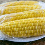 Freezing corn on the cob displayed as golden yellow ears on a white platter with butter melting on top