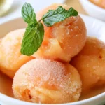 Peach sorbet scooped into a white bowl with fresh peach slices and mint garnish on a marble surface