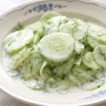 German cucumber salad with creamy dressing and fresh dill served in a white bowl on a wooden table