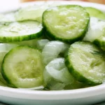 Cucumbers and onions in vinegar served in a white bowl with fresh dill garnish on a wooden table