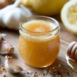 Garlic honey medicine in a glass jar showing fermented garlic cloves suspended in golden honey on a rustic wooden table