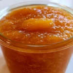 Peach butter recipe in a glass jar with a spoon showing smooth golden spread