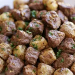 Garlic steak bites and potatoes served in a cast iron skillet with golden crispy potatoes and tender beef cubes