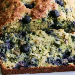 Blueberry zucchini bread sliced on a wooden board showing moist crumb with fresh blueberries
