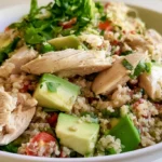 Chicken and quinoa bowl with grilled sliced chicken, fluffy quinoa, cherry tomatoes, cucumber, and bell peppers in a white bowl