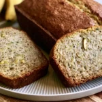 Banana zucchini bread sliced on a wooden board showing moist tender crumb