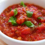 Roasted tomato sauce in a white bowl with fresh basil garnish on a wooden table