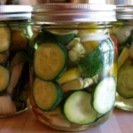 Refrigerator pickles in a glass jar with fresh dill and garlic on a white countertop