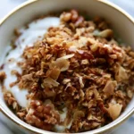 Granola recipe showing golden crunchy clusters in a white bowl with fresh berries
