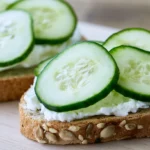 Cucumber sandwiches arranged on white platter with crusts removed and cut into triangles