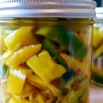 Pickled banana peppers in a glass jar with golden brine and visible spices on a wooden table
