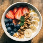 Yogurt bowl with fresh berries, granola, sliced almonds, and honey drizzle in a white ceramic bowl