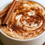 Pumpkin spice latte in a white ceramic mug topped with whipped cream and cinnamon on a rustic wooden table