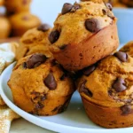 Pumpkin chocolate chip muffins with golden domed tops and visible chocolate chips on a white plate