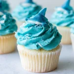 Shark attack cupcakes with blue buttercream waves and gummy sharks on white plate