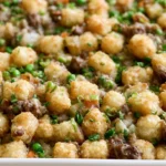 Tater tot casserole recipe with golden crispy tots, melted cheese, and seasoned ground beef in a white baking dish