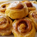 Pumpkin cinnamon rolls with cream cheese glaze on a white plate, showing soft fluffy texture and spiral layers
