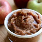 Apple butter recipe in a glass jar with a spoon showing thick, dark caramelized spread