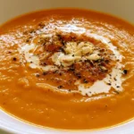 Roasted Apple Pumpkin Soup in a white bowl with cream swirl and pumpkin seeds on rustic wooden table