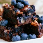 Fresh blueberry brownies stacked on white plate showing fudgy chocolate texture with purple berry swirls