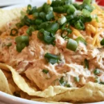 Texas trash dip in a white bowl surrounded by tortilla chips and garnished with green onions
