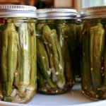 Pickled okra in a clear glass jar showing crisp green pods with garlic and red pepper flakes