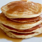 Buttermilk pancake recipe stacked on a white plate with butter and maple syrup