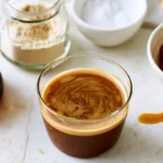 Pumpkin coffee syrup in a glass jar next to a cup of coffee with fall spices