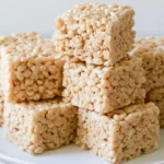 Gingerbread Rice Krispie Treats cut into squares on a white plate with holiday decorations
