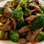 Beef and broccoli served over white rice on a white plate with glossy sauce coating the tender beef slices and bright green broccoli florets