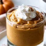 Pumpkin sauce for coffee in a glass jar with a spoon, surrounded by coffee cups and fall spices
