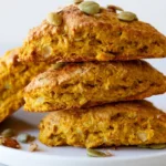 Pumpkin scones with spiced glaze arranged on a white plate with fall leaves in the background