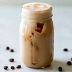 Coffee creamer in a glass bottle next to a cup of coffee on a kitchen counter
