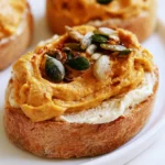Pumpkin cream cheese spread on a toasted bagel with visible orange color and smooth texture