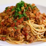 Spaghetti sauce recipe served over cooked spaghetti on a white plate with fresh basil garnish