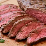 London broil sliced thin against the grain on a white platter showing tender, juicy medium-rare beef