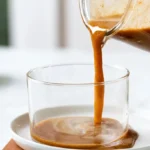 Pumpkin spice syrup in a glass bottle with fall spices and coffee cup on wooden table