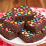 Cosmic brownie recipe with glossy chocolate ganache and rainbow candy chips on a white plate