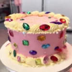 gem cake with glossy mirror glaze and decorative gem accents on white cake stand