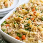Tuna noodle casserole in a white baking dish with golden breadcrumb topping and visible peas